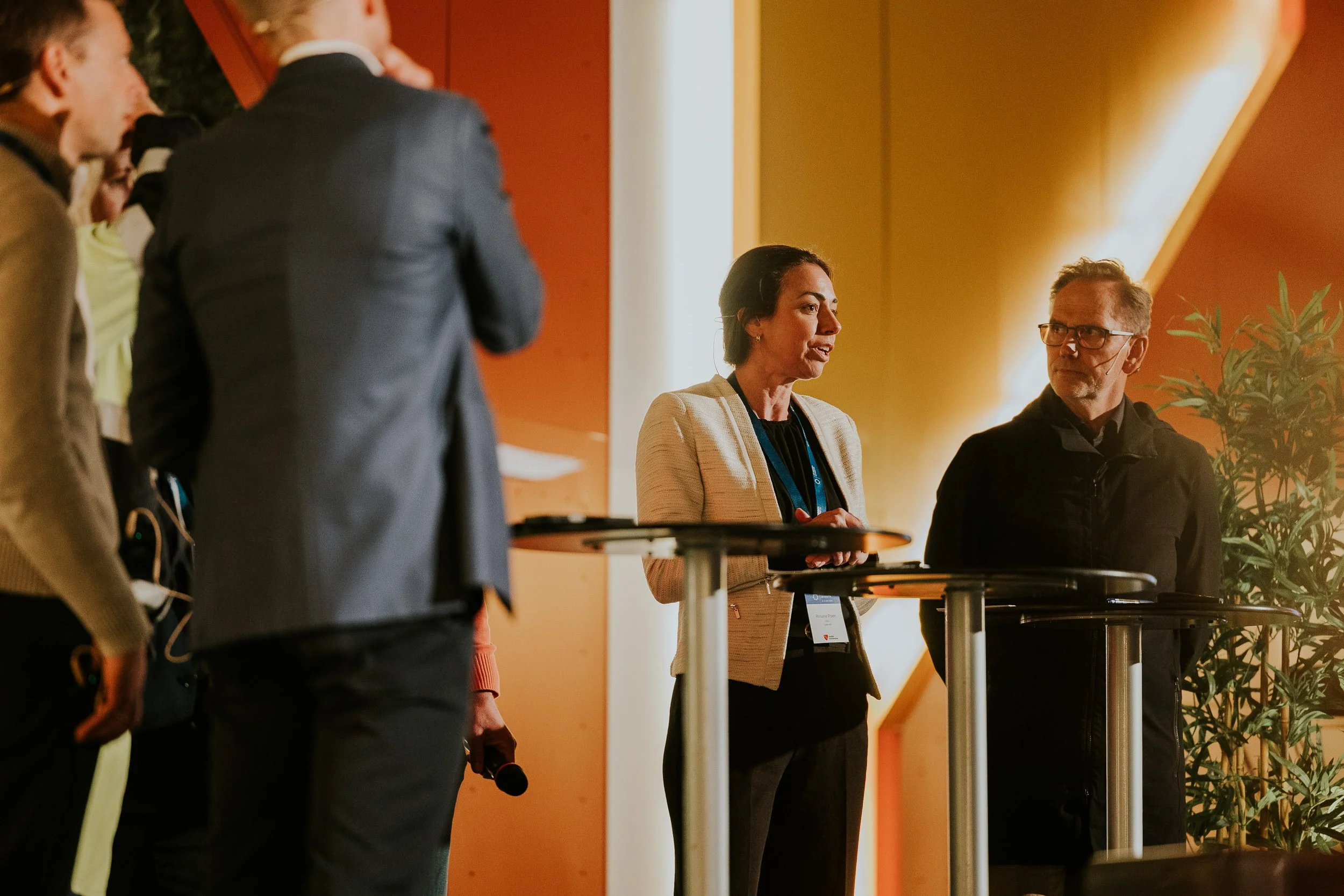 Kvinner og menn i samtale på en konferanse, med noen som snakker og andre som lytter.