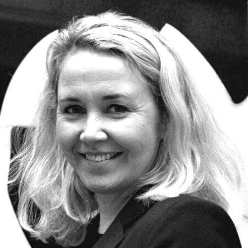 Et svart-hvitt bilde av en smilende kvinne med lyse krøllete hår, som ser mot kamera.
