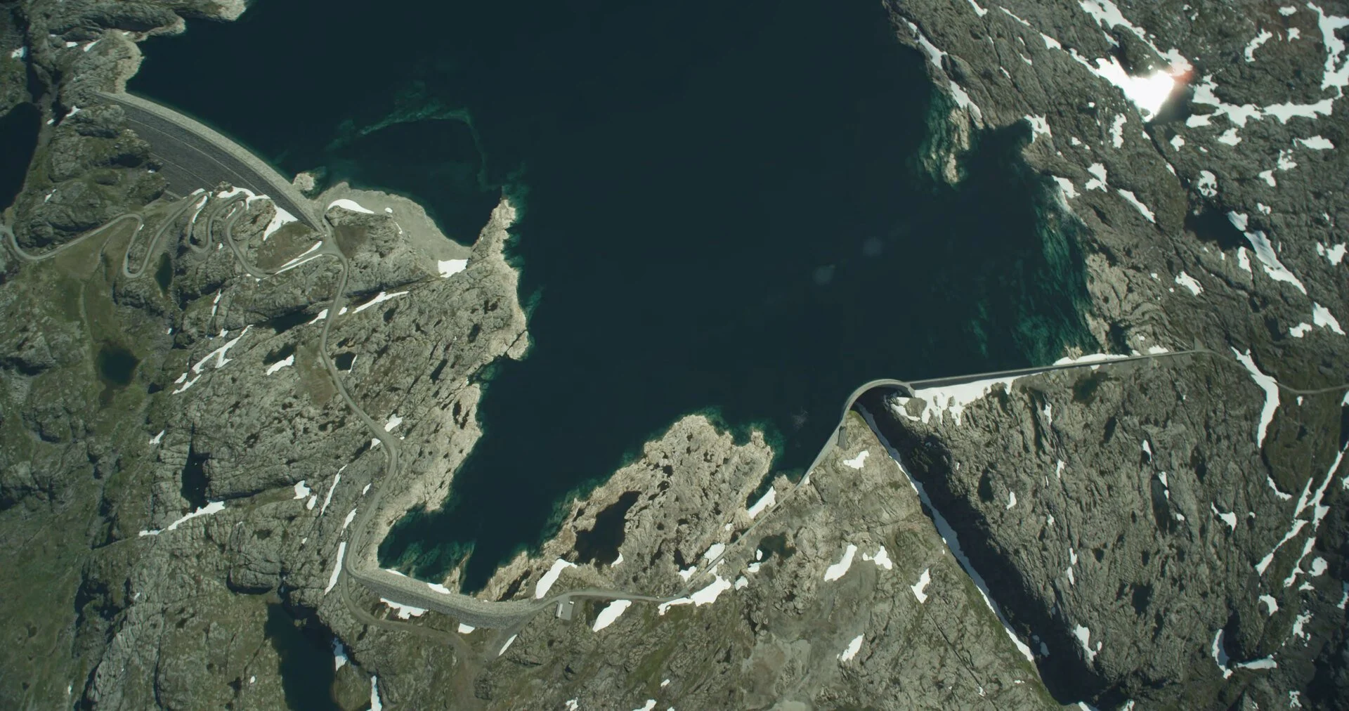 Aerial view of a fjord with steep, rocky cliffs and winding road along the edge.