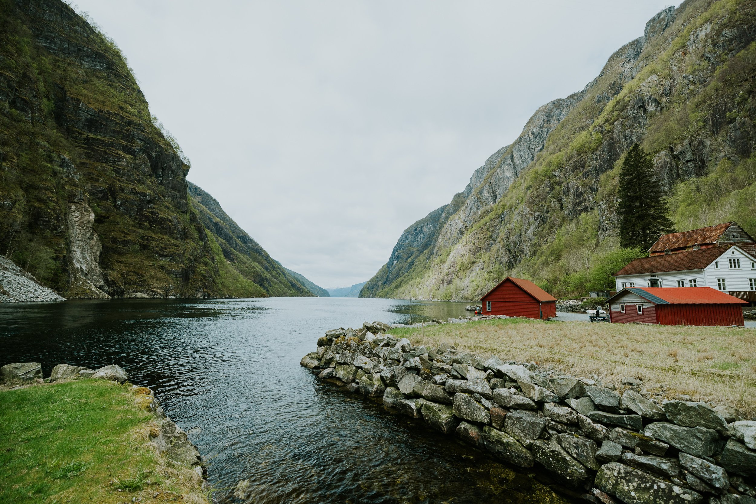 Bilde av en fjord med høye fjell på begge sider og to små hus nær vannkanten.
