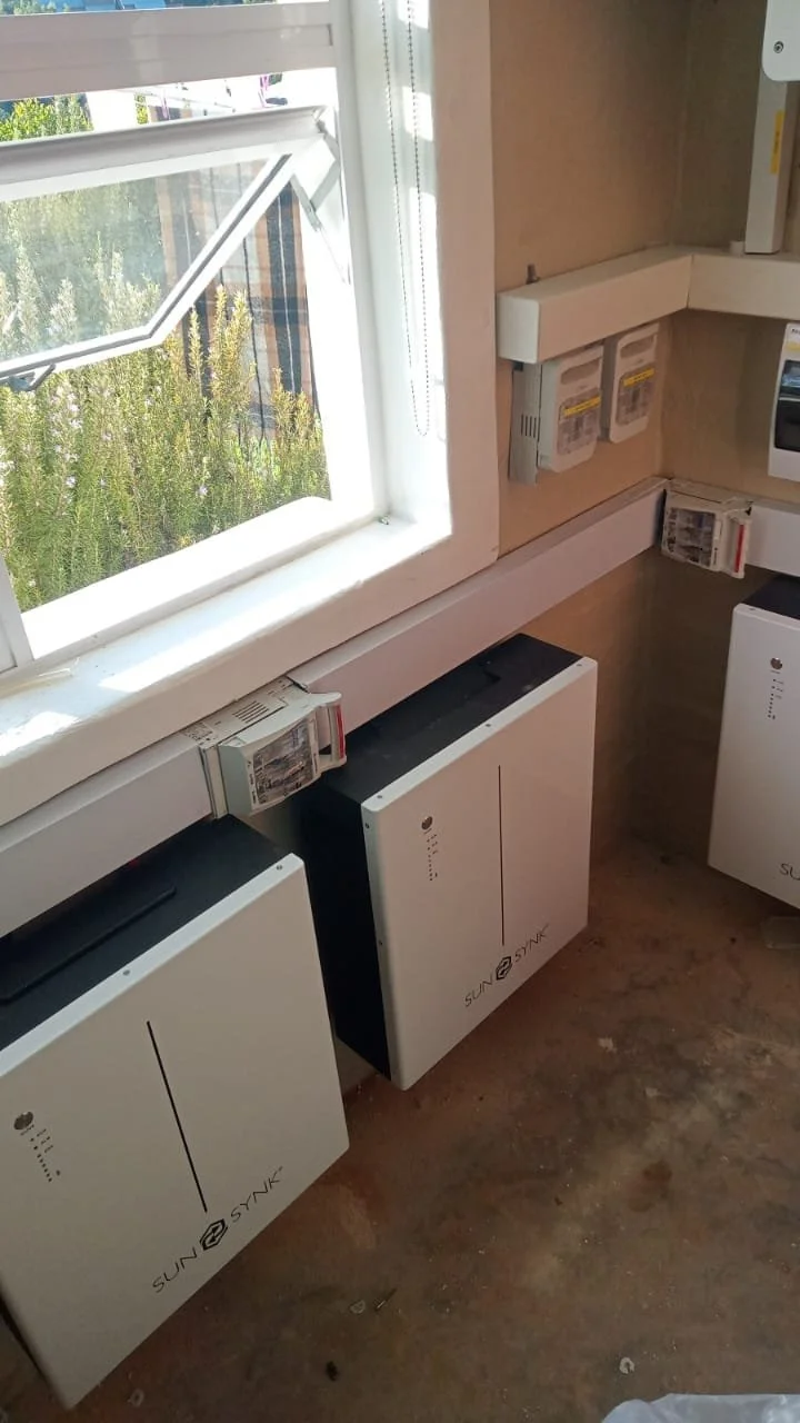 Three solar power inverters installed on a wall in a room with a window.