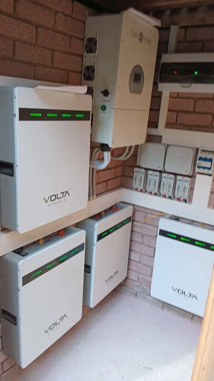 Multiple solar energy inverters and charge controllers mounted on a brick wall in a utility room.