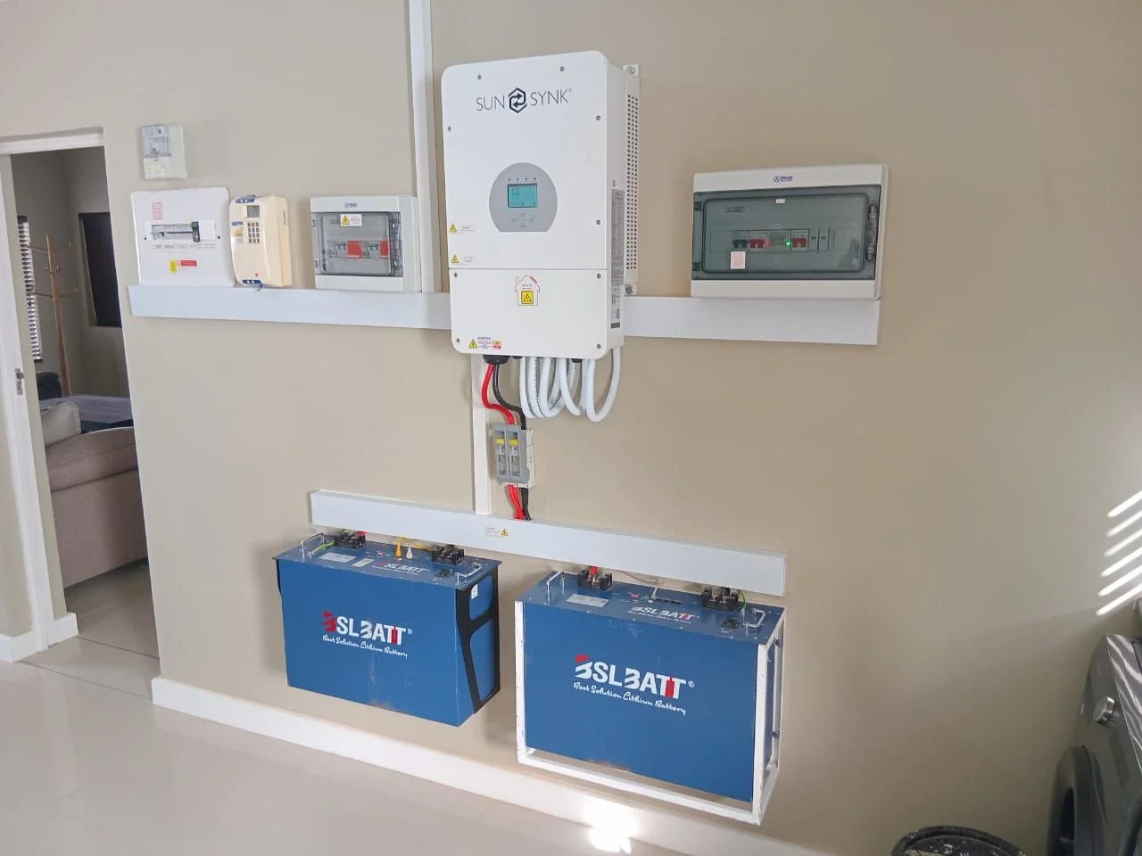Electrical system setup with solar inverter, batteries, and control panels mounted on a beige wall in a residential space.