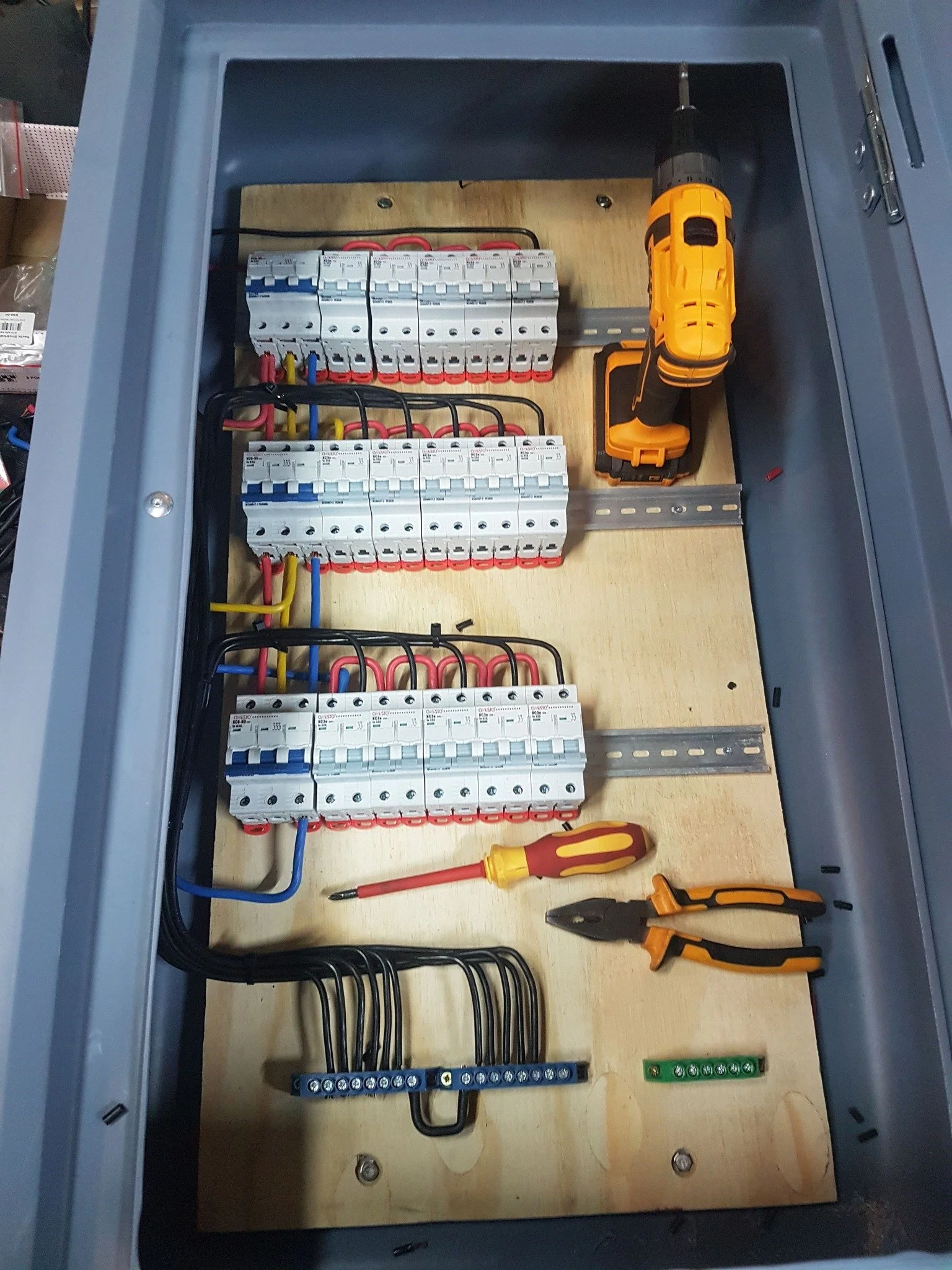 Electrical breaker panel with multiple circuit breakers, screwdriver, pliers, and power drill inside.