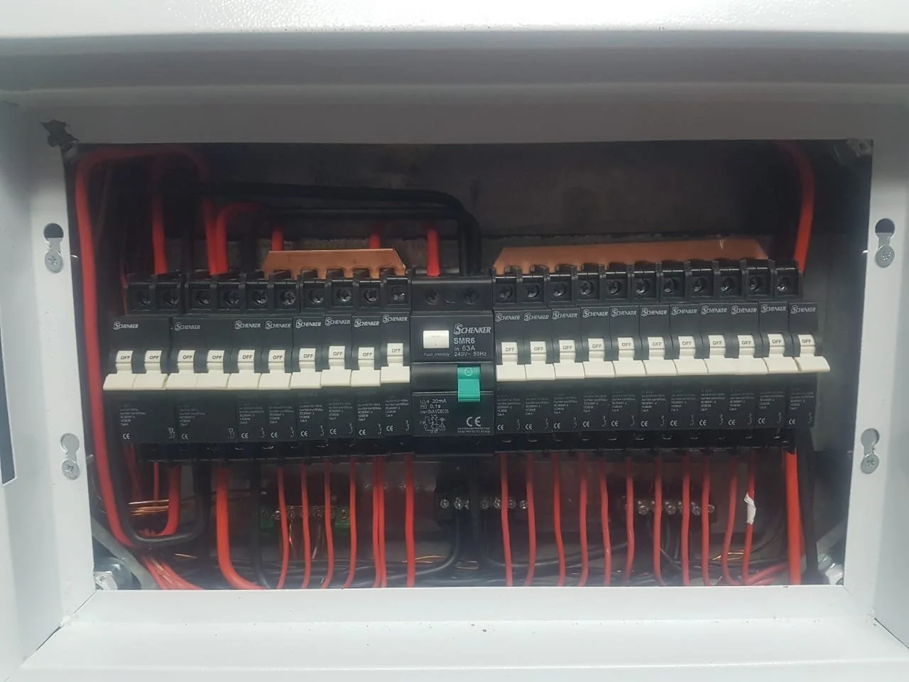 Electrical circuit breaker panel with multiple switches and red wiring.
