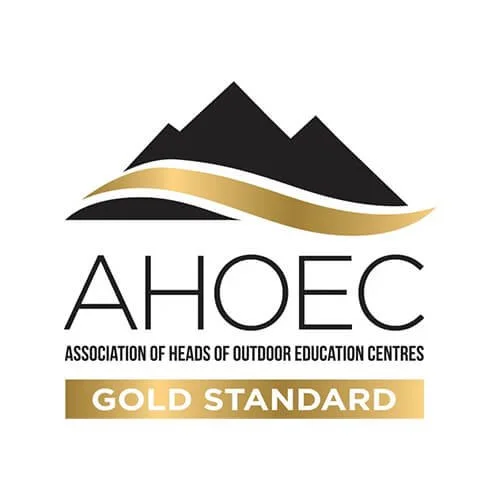 Logo of the Association of Heads of Outdoor Education Centres (AHOEC), featuring a mountain and a gold-colored ribbon with text indicating a Gold Standard certification.