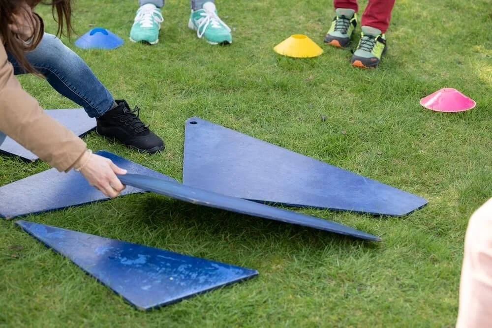 People assembling a blue glider on a grassy field with colored cones marking spots.