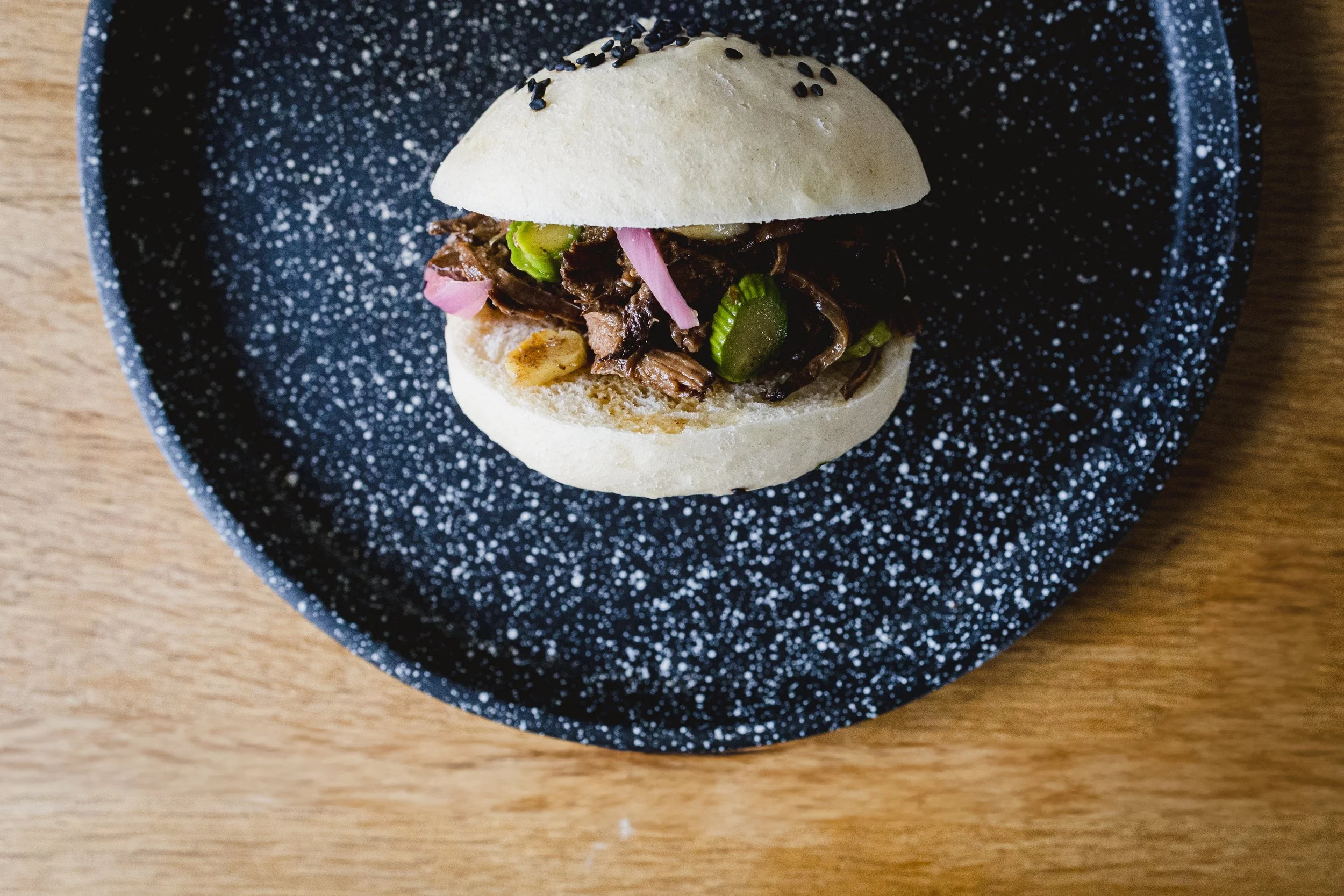 Burger revisité par Chelle Lorette avec un bao et de l’effiloché de porc, mis en scène dans une photographie food graphique et colorée