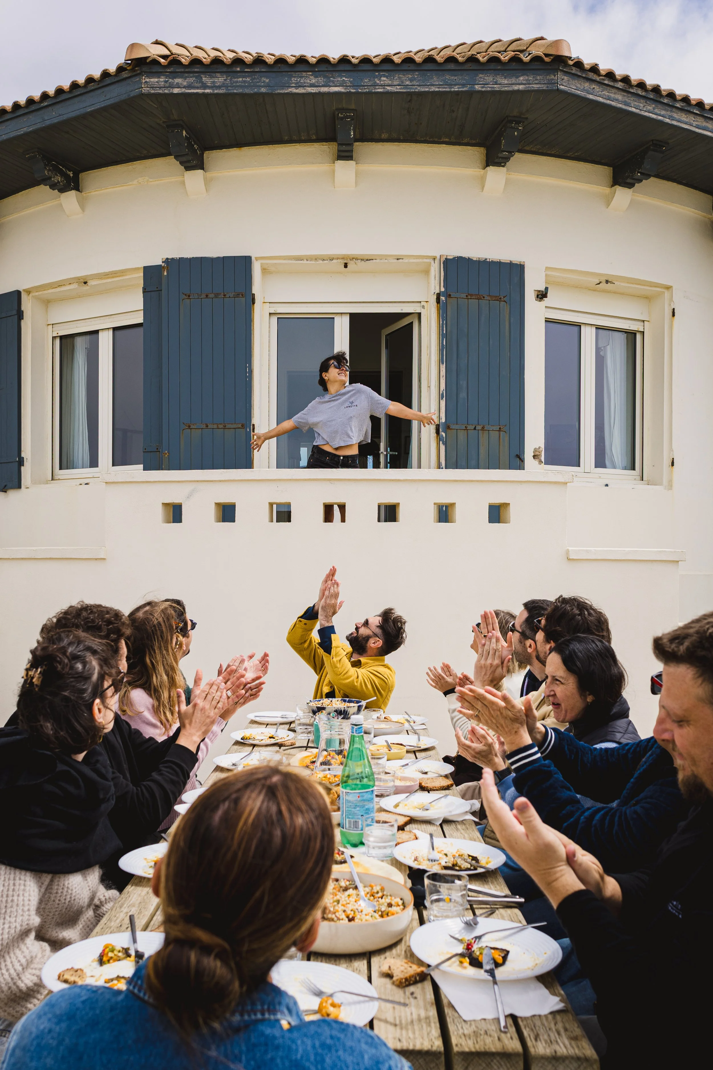 Une cheffe cuisinière reçoit les applaudissements d’une tablée lors d’un workshop culinaire, dans une ambiance chaleureuse et vivante