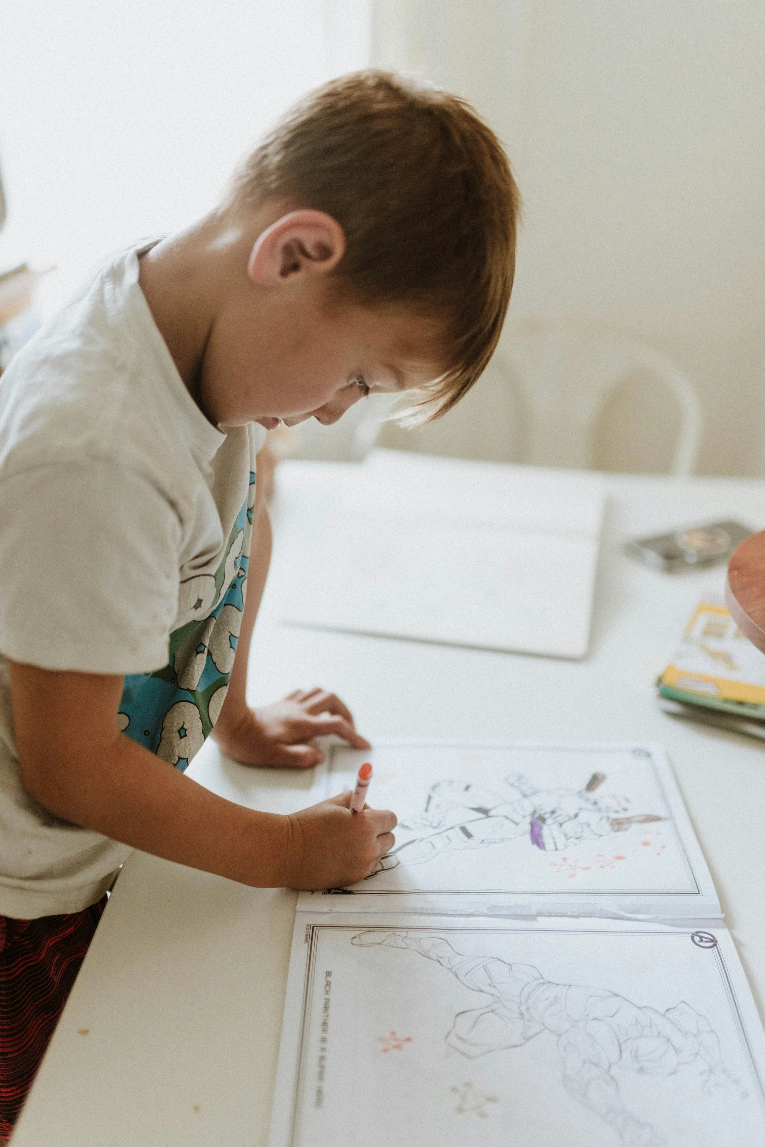 Un garçon qui colorie une page de livre de coloriage sur une table blanche, avec des dessins d'anatomie humaine, dans une pièce lumineuse.