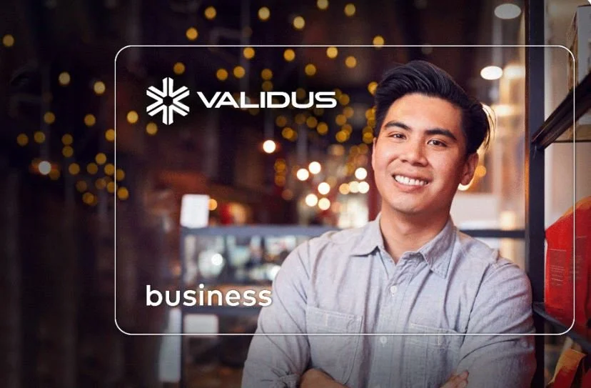 A smiling young man standing with arms crossed in an urban setting at night, with warm string lights in the background. Overlay text includes the logo and name 'VALIDUS' and the word 'business'.