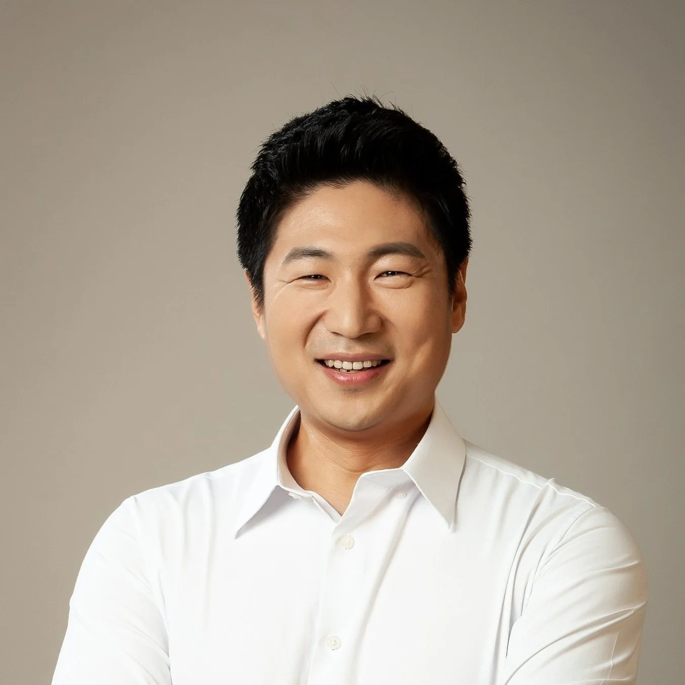 Smiling man with black hair wearing a white dress shirt against a plain background.