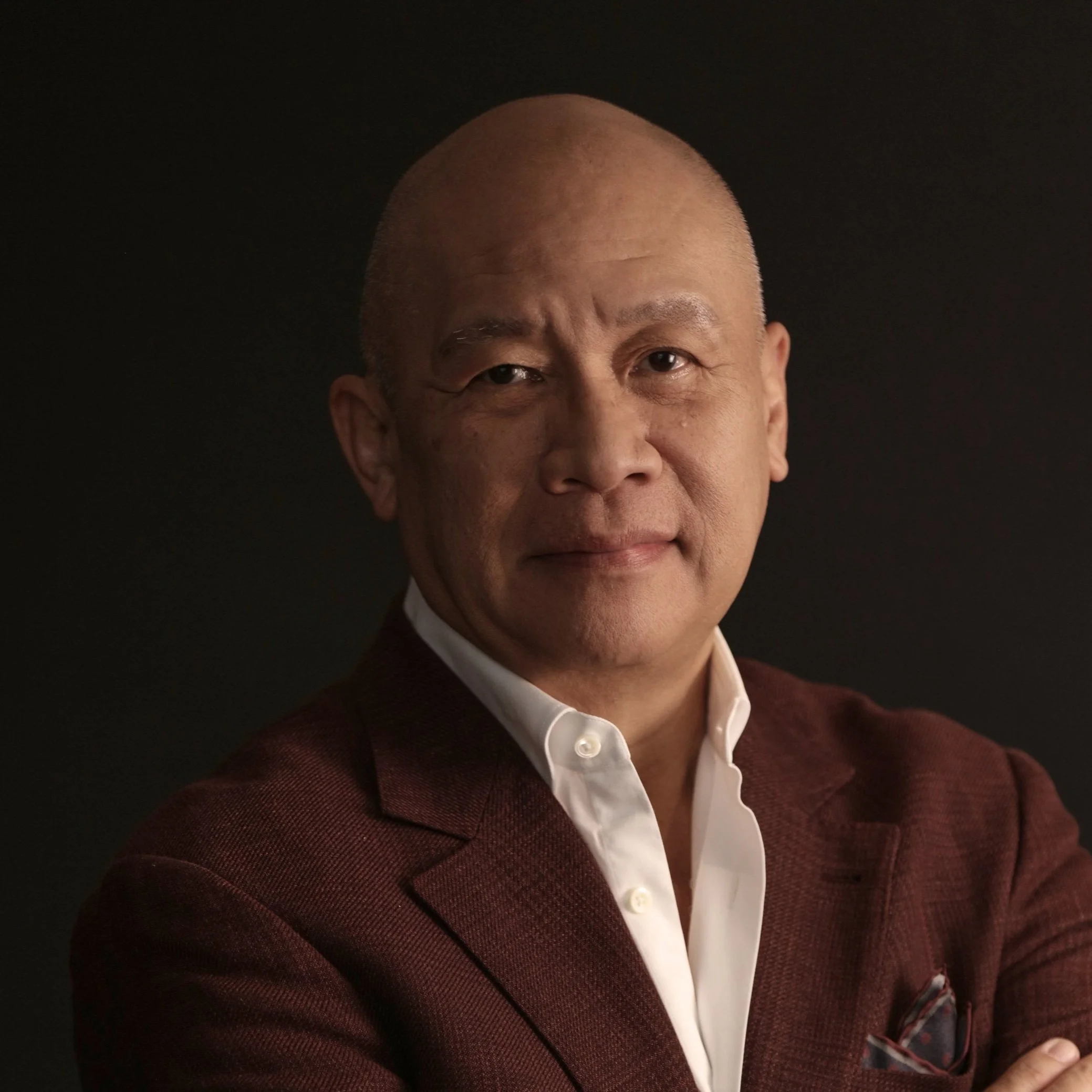 Portrait of a bald Asian man in a suit against a dark background