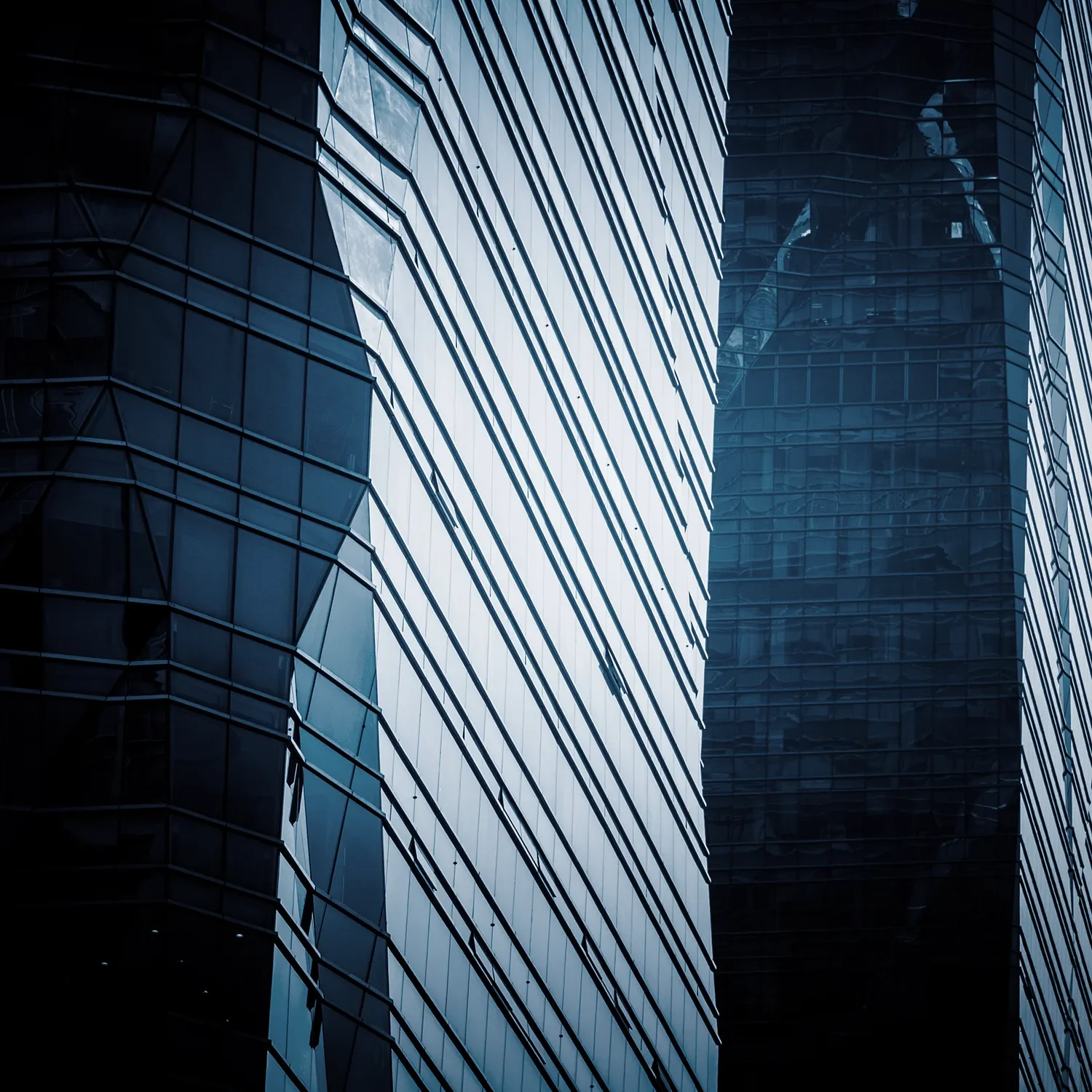 Close-up of modern glass skyscrapers reflecting the sky and surrounding buildings, with geometric patterns.