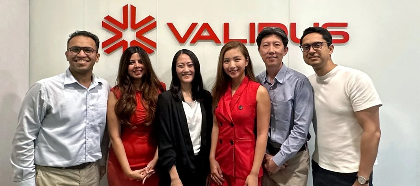 Six people standing side by side in front of a wall with a red logo and the word 'VALIOUS'. They are smiling and dressed in business casual attire.