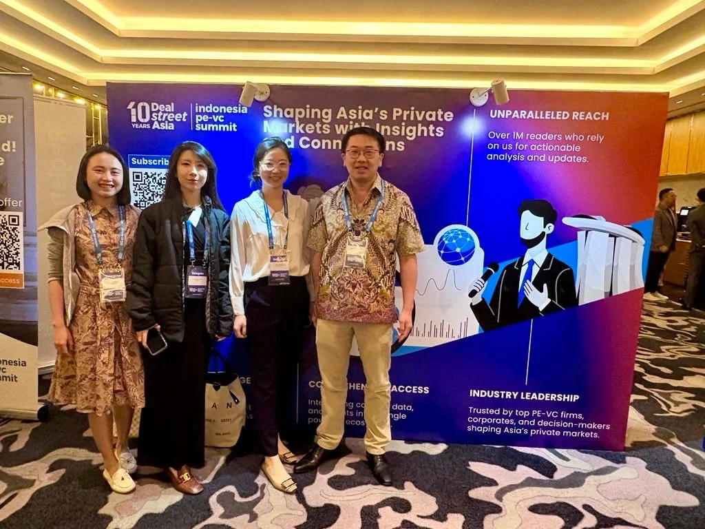 Four people standing in front of a promotional display at a conference, with the display mentioning Asia's private markets and insights.