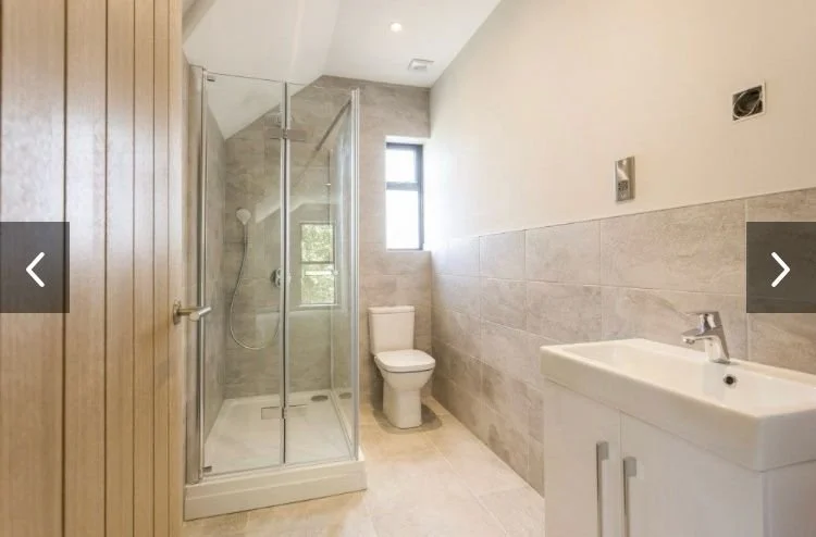Modern bathroom with walk-in shower, toilet, and sink, featuring neutral-colored tiles and a small window.