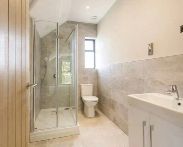 Bathroom with glass shower enclosure, toilet, small window, and white sink with cabinet