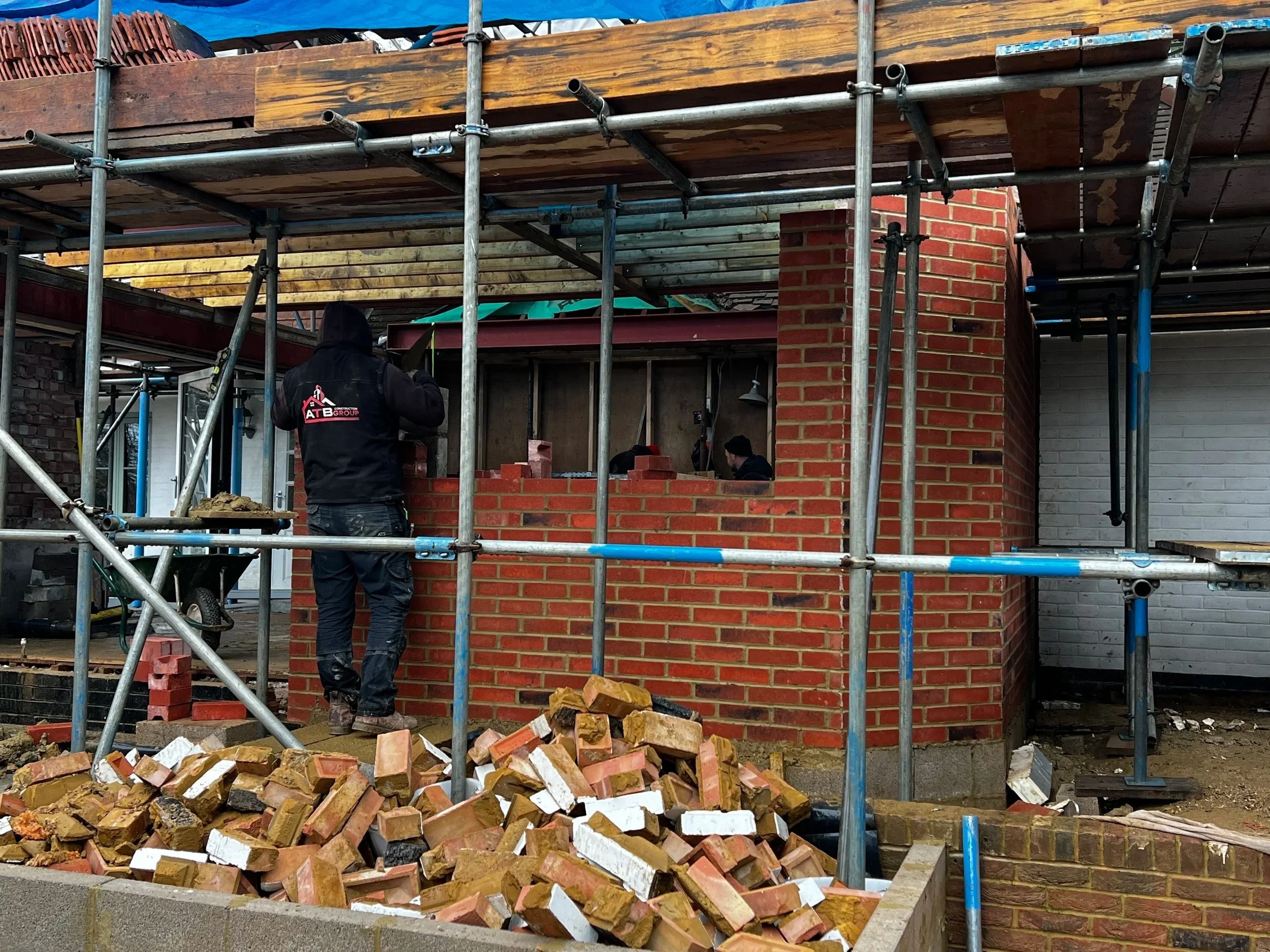 Workers building a brick house with scaffolding and construction materials around.