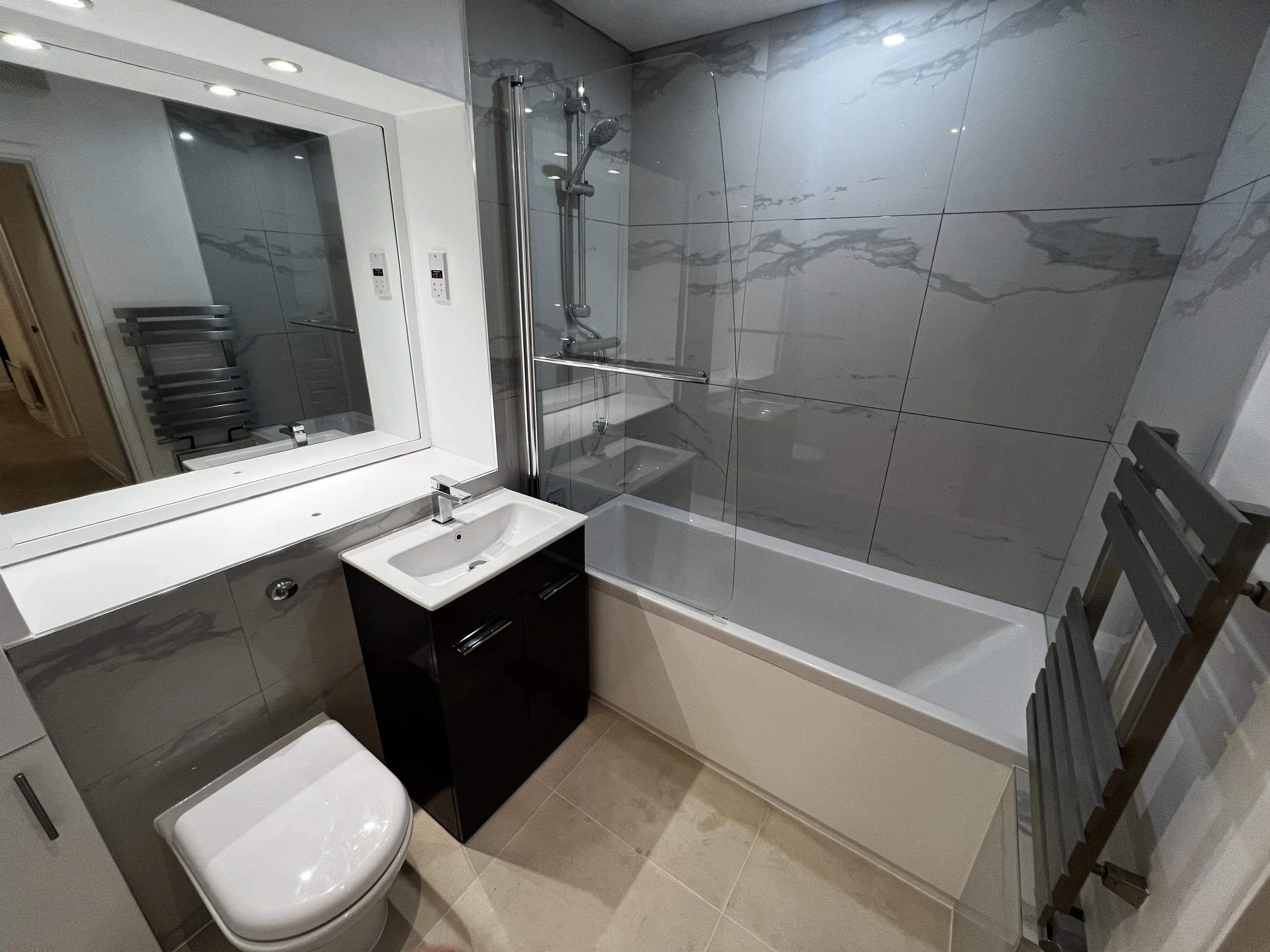 A modern bathroom with a glass shower enclosure, marble-look tiles, a white toilet, a black vanity with a white sink, and a mirror.