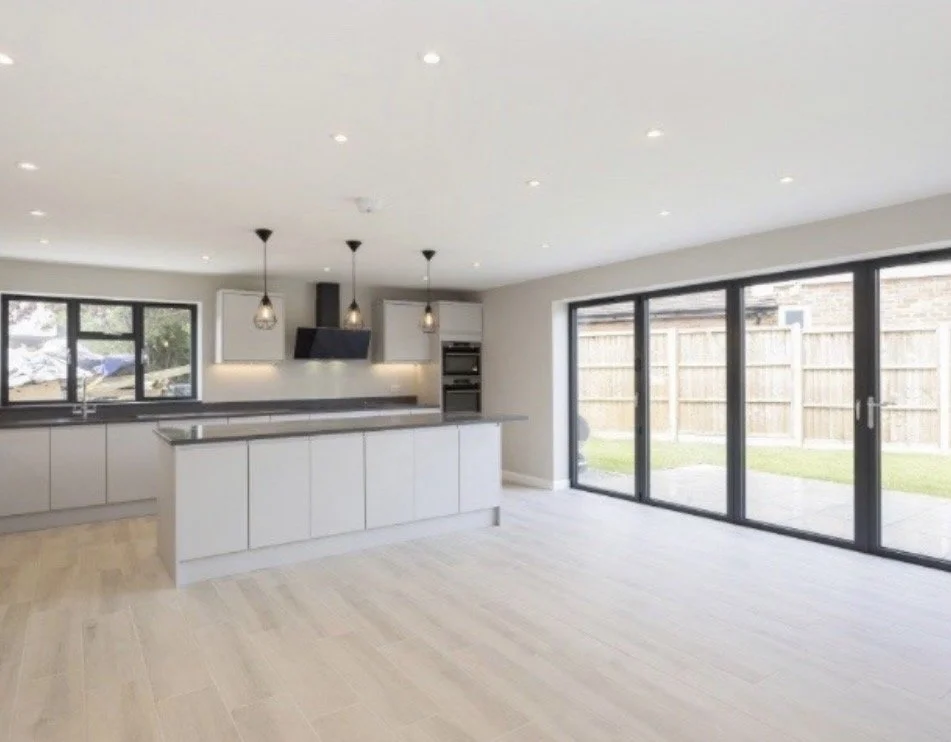 Modern open-concept kitchen with white cabinets, a breakfast bar, pendant lighting, large sliding glass doors, and a view of a backyard with a wooden fence.