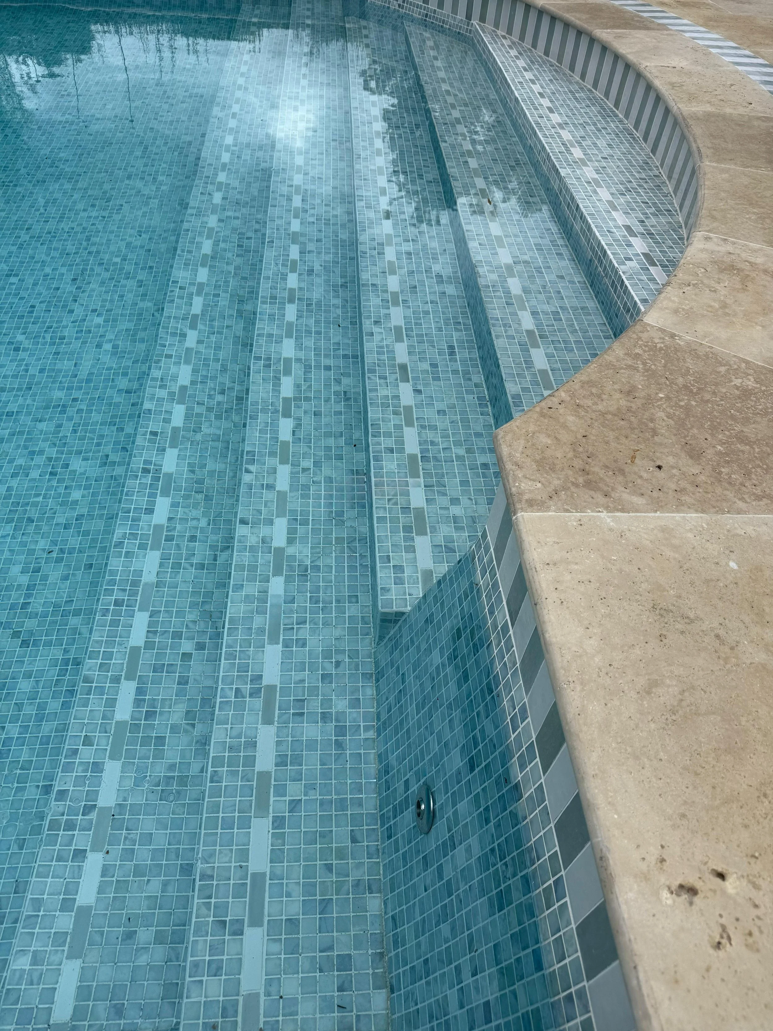 Close-up of an empty swimming pool with blue tiled interior, a built-in step, and a concrete deck surrounding it.