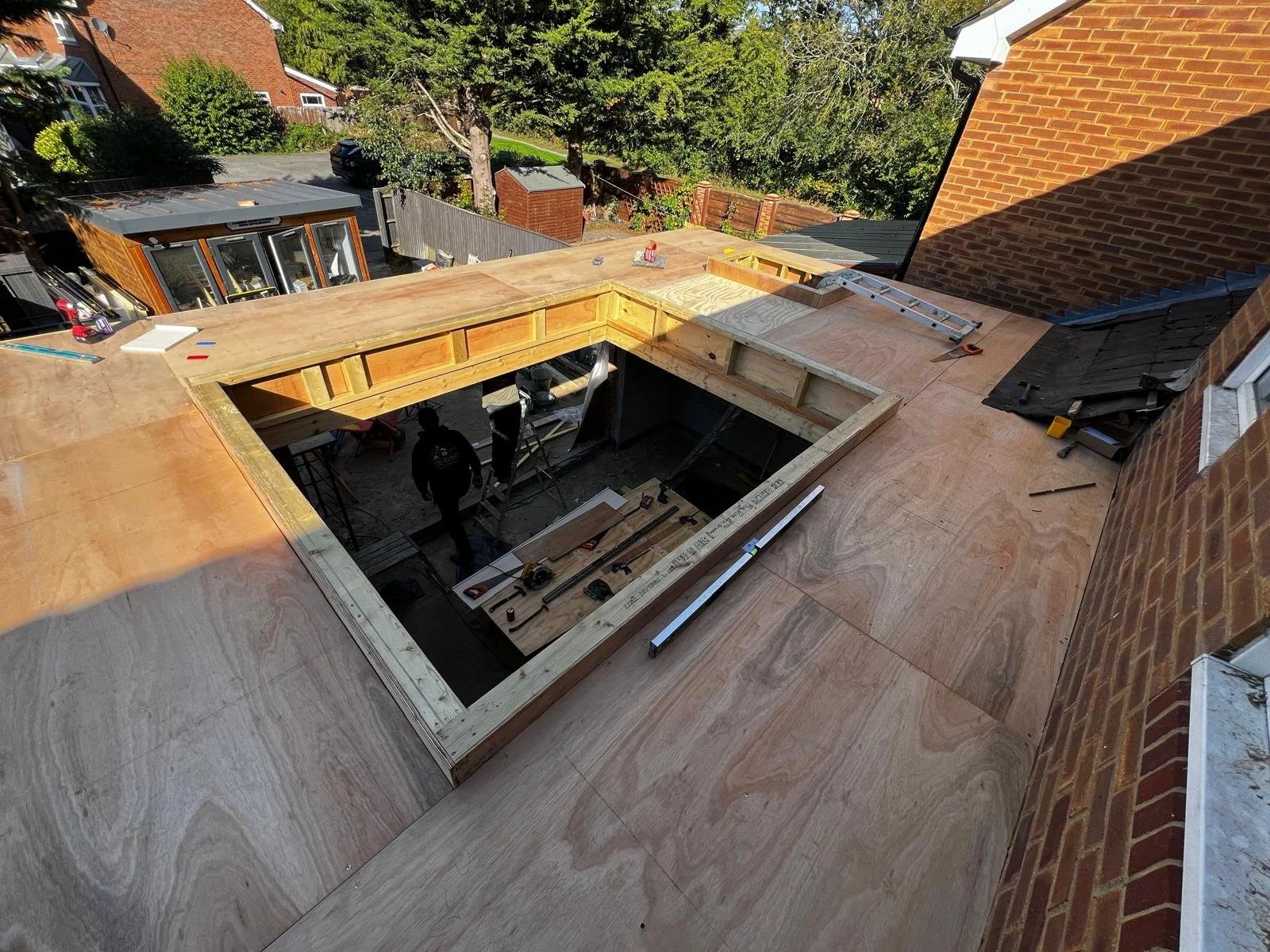 Construction workers installing a new roof with plywood on top of a building, with tools and materials scattered around.