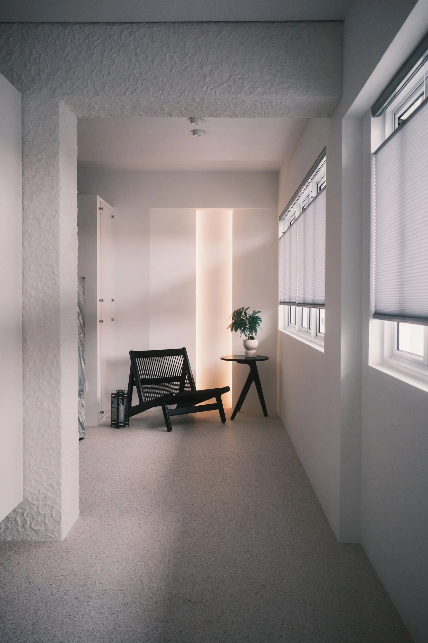 Honeycomb blinds softly filtering natural light in a bright minimalist corner with textured walls and a lounge chair.