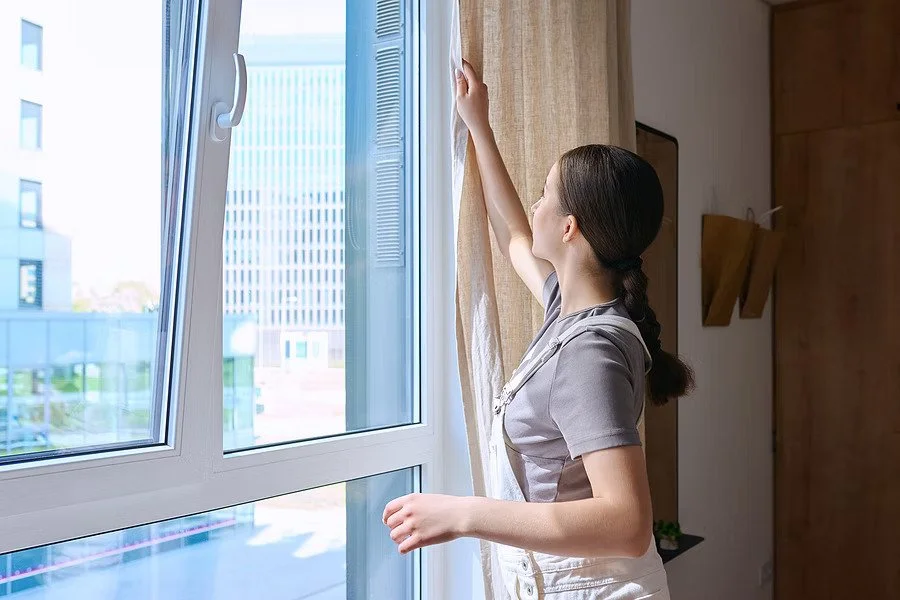 Everyday Curtains Singapore window treatment in a bright room, with a person adjusting beige curtains beside large windows for privacy and natural light control.