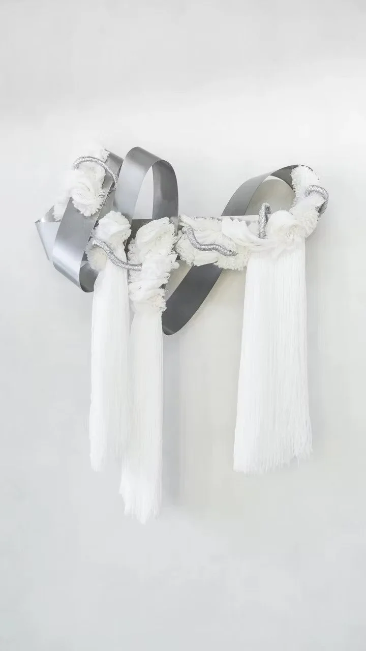Curtains Singapore close-up of contemporary fibre art made with white textured fabric, tassels, and silver sculptural forms on a neutral wall.