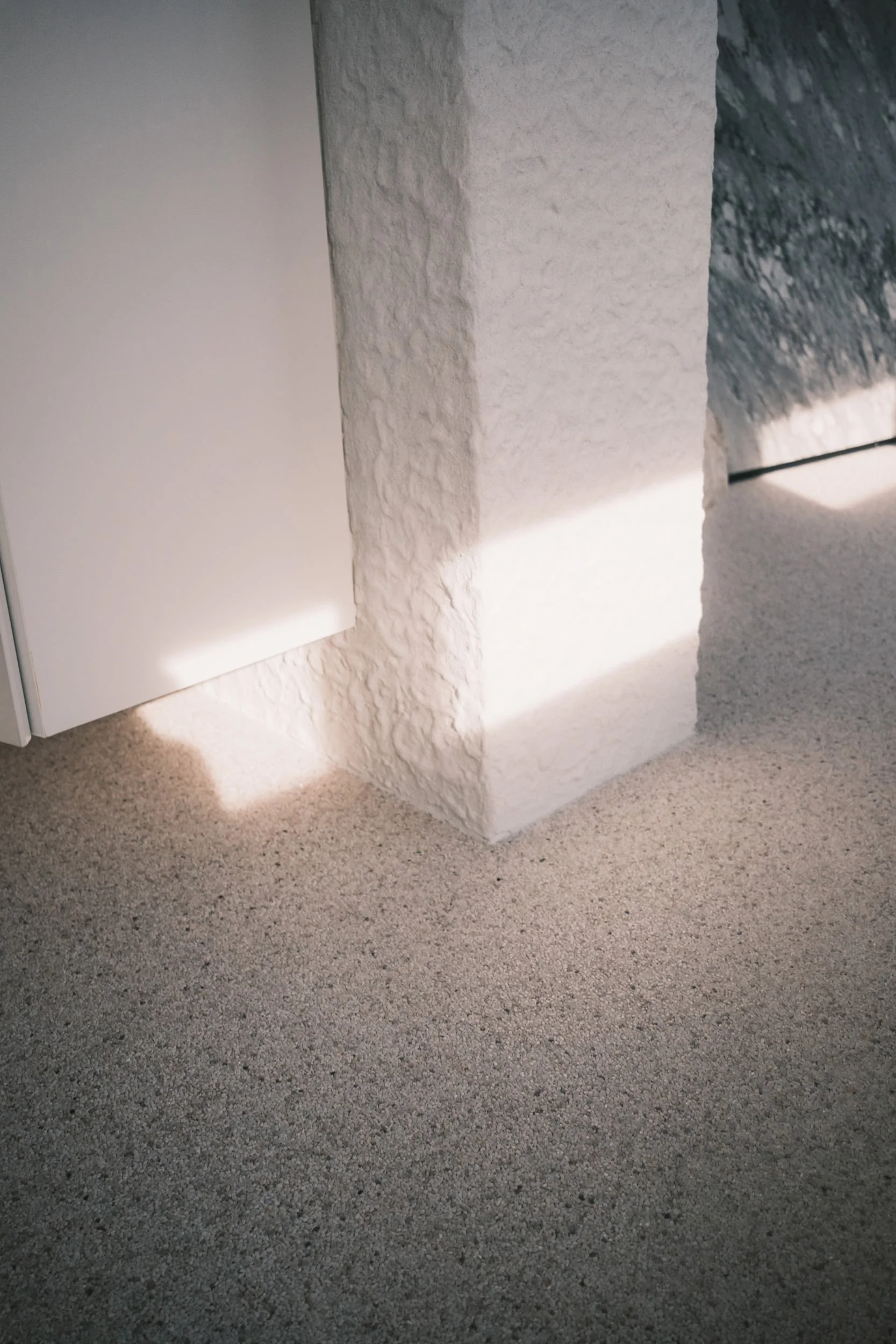 Sunlight shaped by honeycomb blinds, casting soft lines across a textured wall and floor in a minimalist interior.