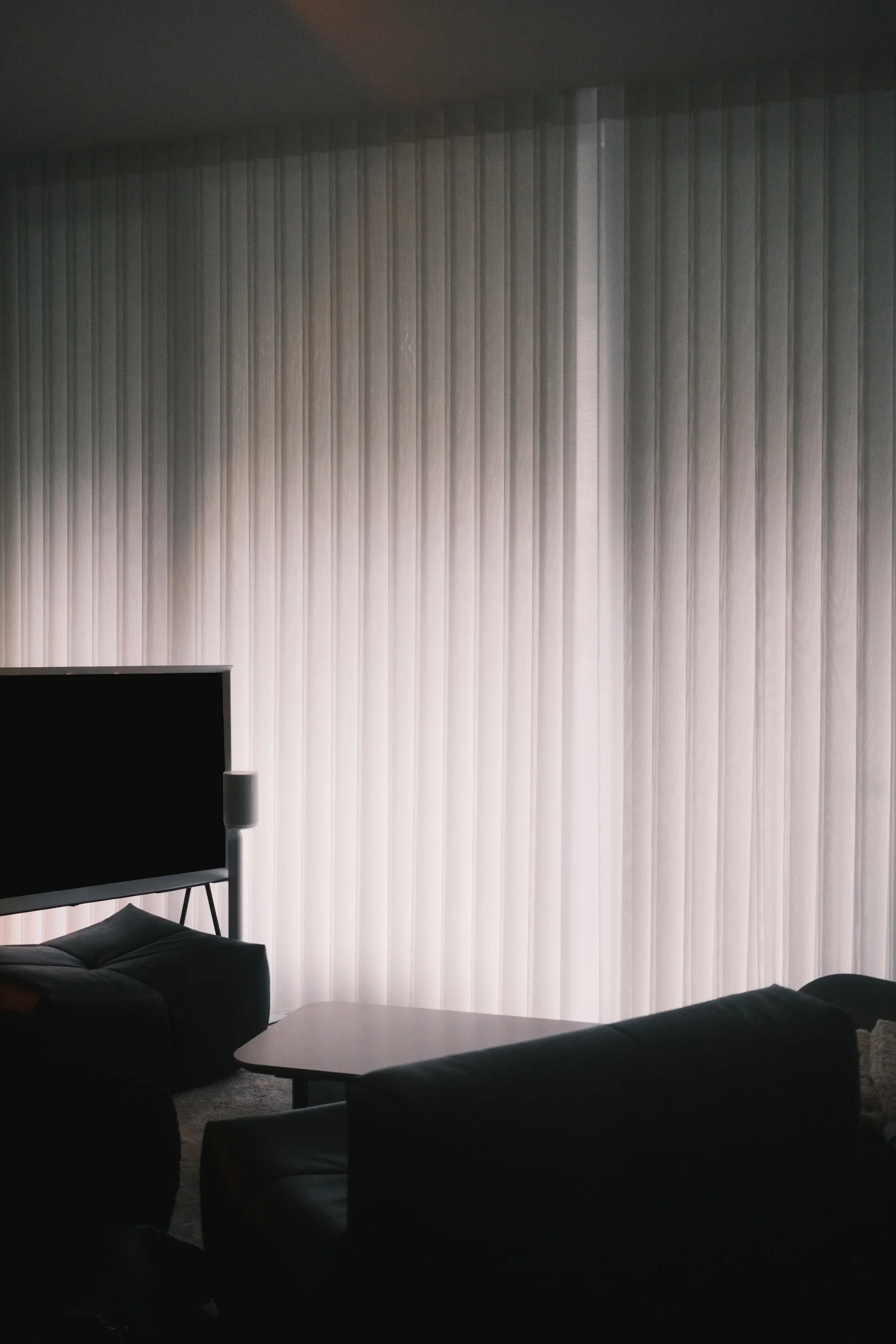 Full-height ripple blinds softly filtering natural light in a modern living room with dark furniture.