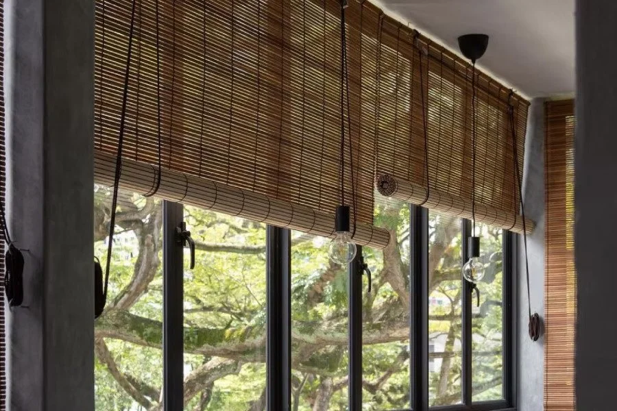Curtains Singapore bamboo blinds installed over black-framed windows, filtering natural daylight with a warm wooden texture.