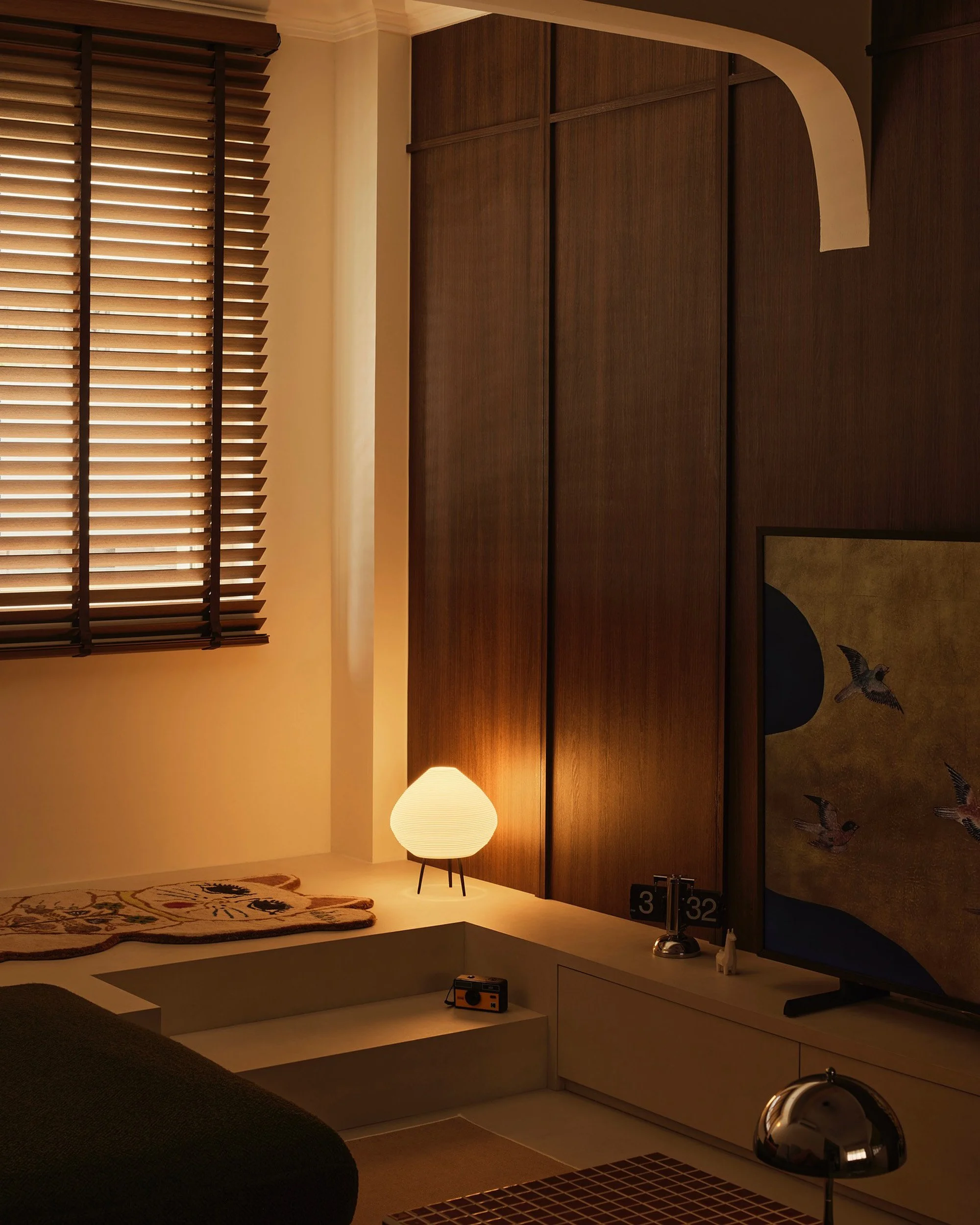 Venetian blinds filtering warm light in a cosy Singapore living room with dark wood accents and ambient lighting.