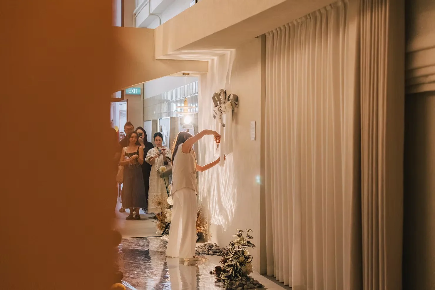 Curtains Singapore contemporary fibre art installation beside full-height neutral curtains, with an artist presenting textured fabric work to guests in a warm gallery setting.