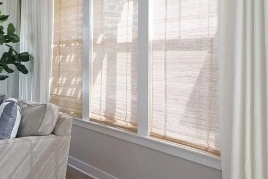 Curtains Singapore woven wood shades on large living room windows, filtering soft daylight with natural woven texture beside neutral curtains.