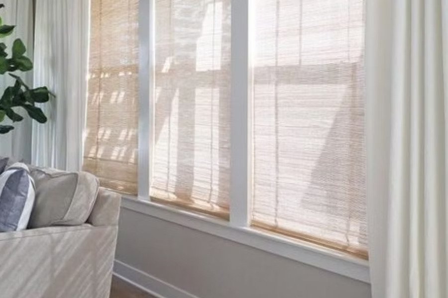 Everyday Curtains Singapore woven wood shades on large living room windows, filtering soft daylight with natural woven texture beside neutral curtains.