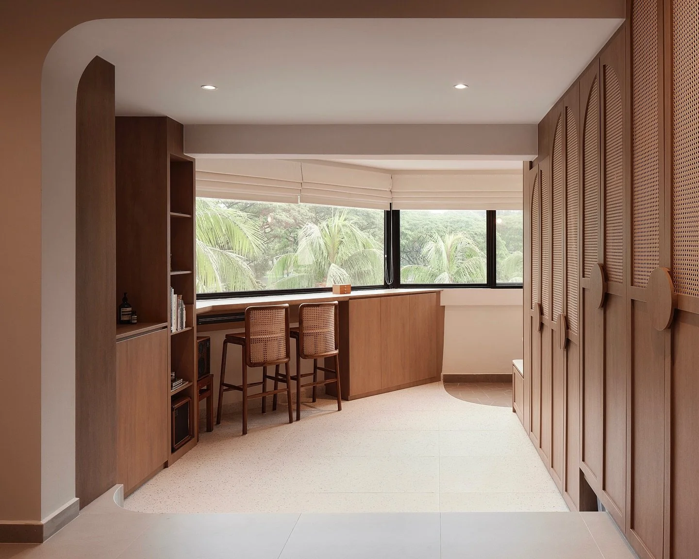 Roman blinds filtering natural light in a Singapore home bar counter area with warm wood finishes and greenery outside.