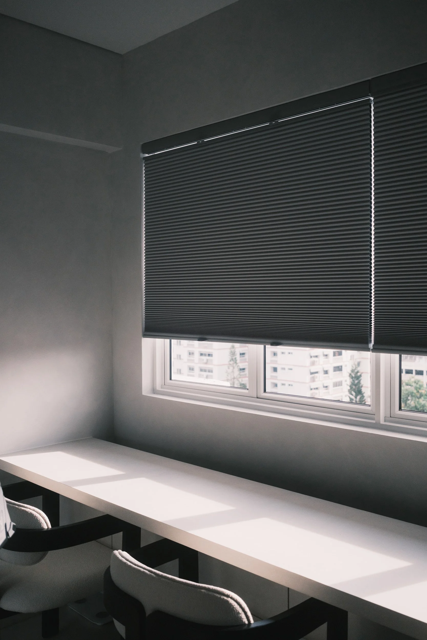 Honeycomb blinds in a Singapore HDB study room, partially covering the window for privacy while allowing natural light to enter and cast soft lines across the study table.