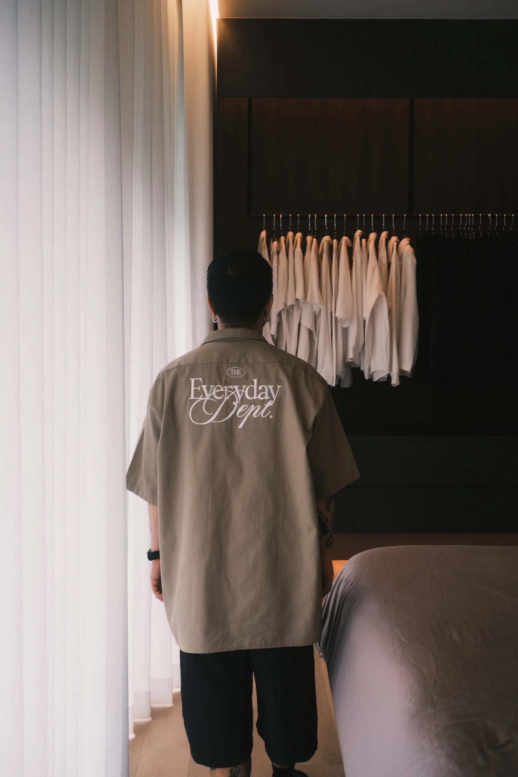 Person standing in a bedroom beside ripple blinds, with soft natural light filtering into a dark wardrobe space.