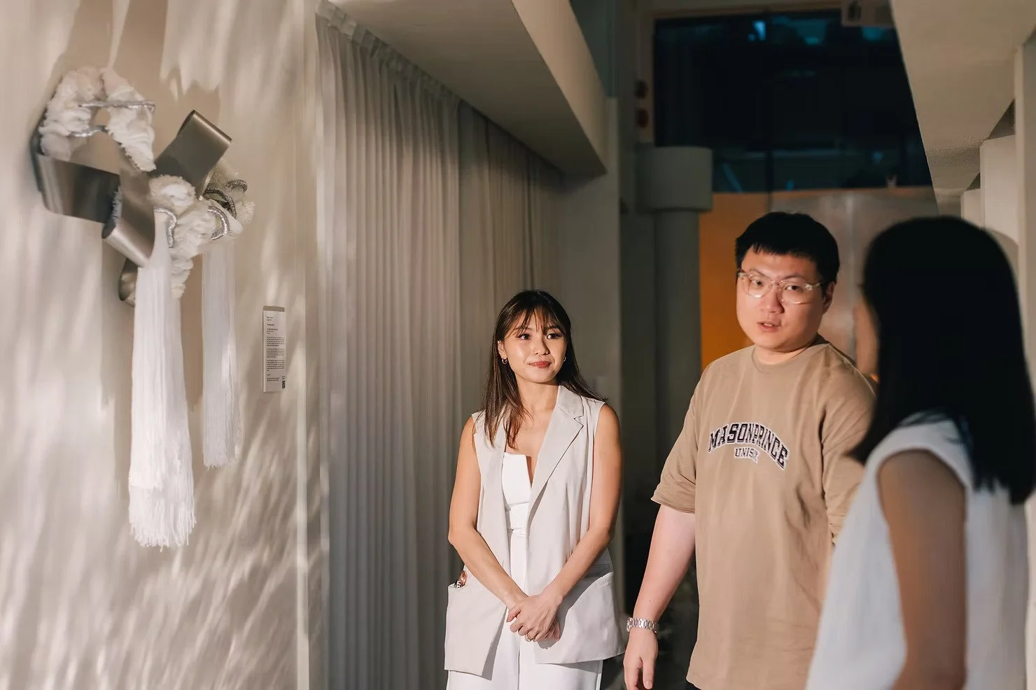 Curtains Singapore fibre art installation beside full-height neutral curtains, with guests viewing textured fabric artwork in a warm gallery interior.
