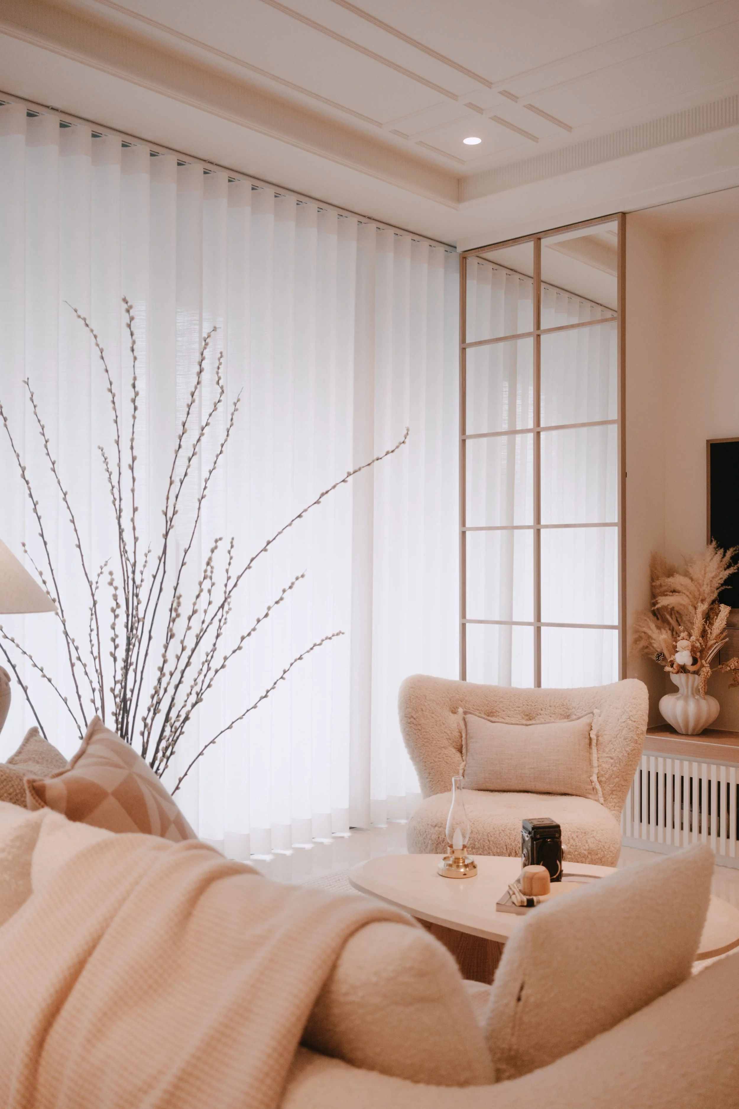 Ripple Blinds filtering daylight in a soft neutral living area, complementing the curved armchair, cream-toned palette and delicate decorative branches.