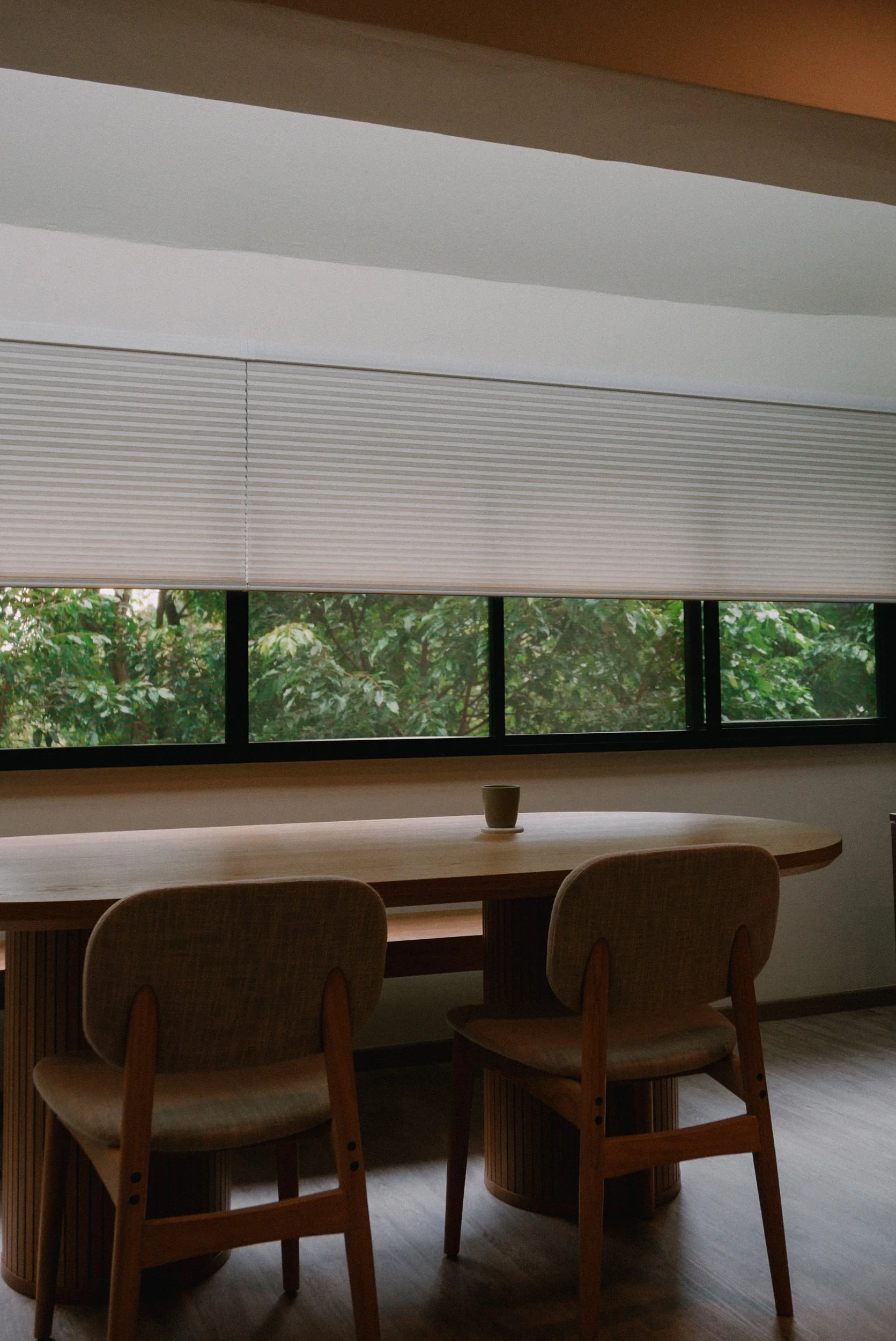Honeycomb blinds partially lowered in a Singapore dining area, framing the greenery outside while adding privacy and soft light control.