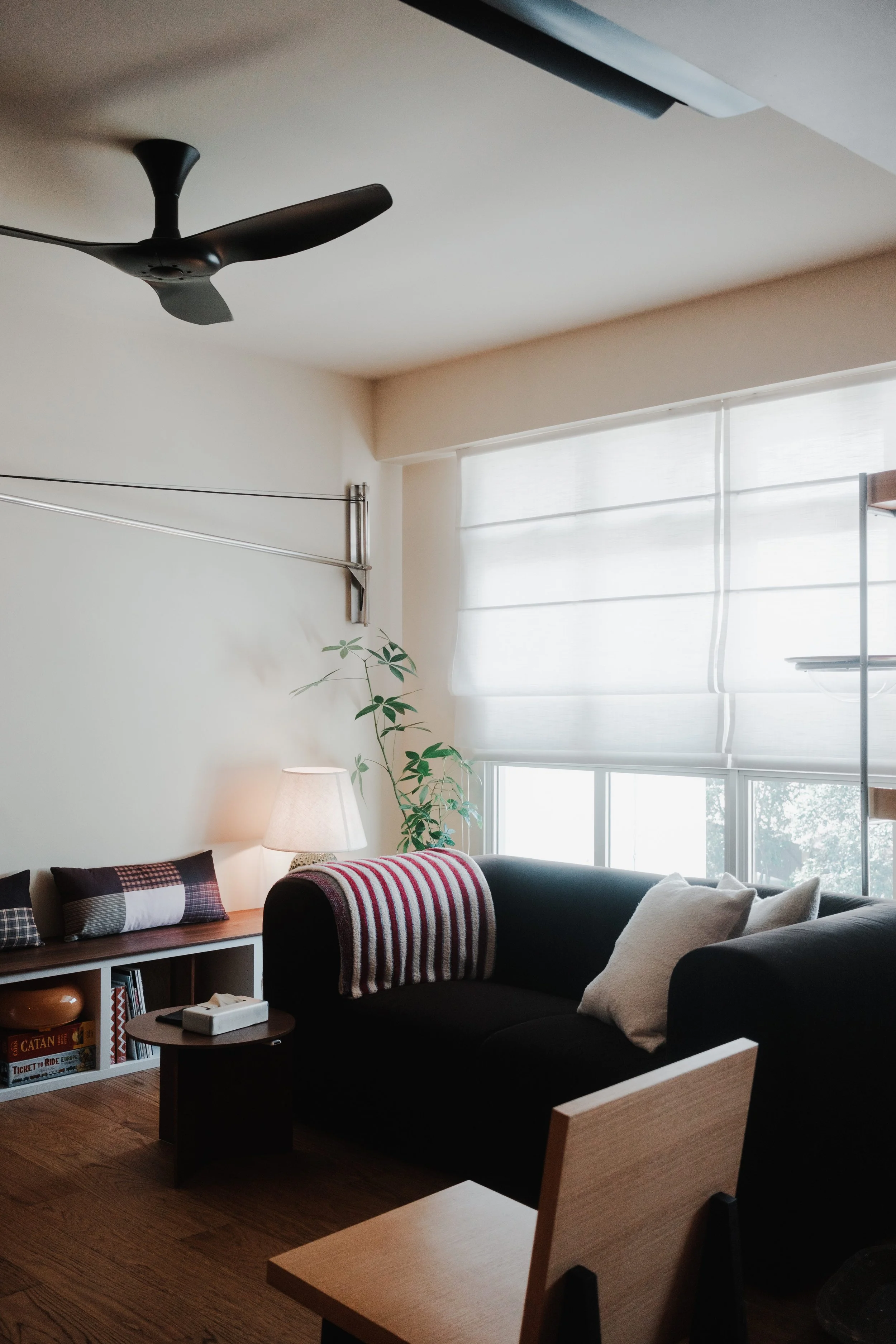 Roman blinds filtering natural light in a cosy Singapore living room, with wooden furniture, collectibles and cosy couch.