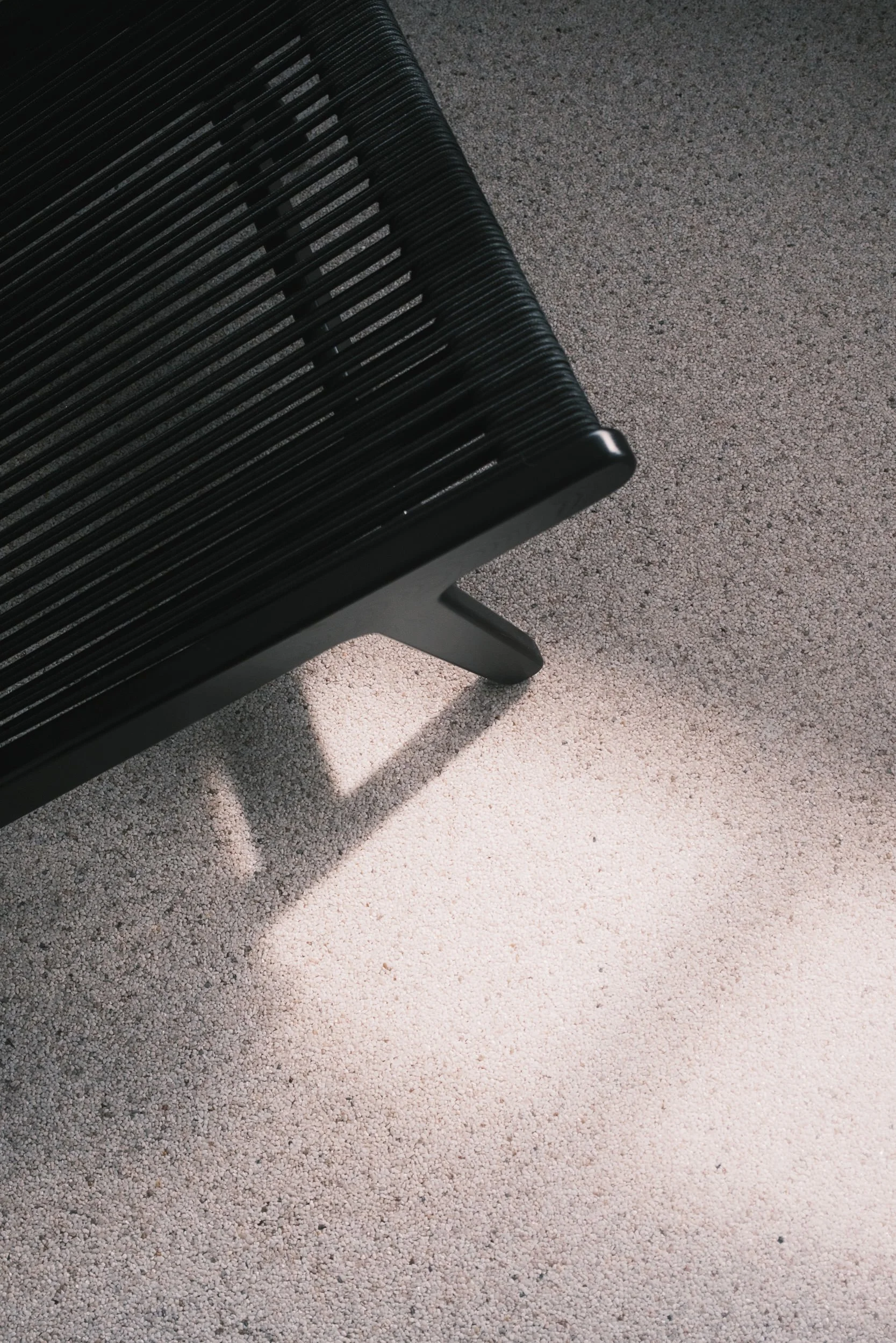Sunlight shaped by honeycomb blinds, casting soft lines across a textured floor and wooden lounge chair in a minimalist interior.