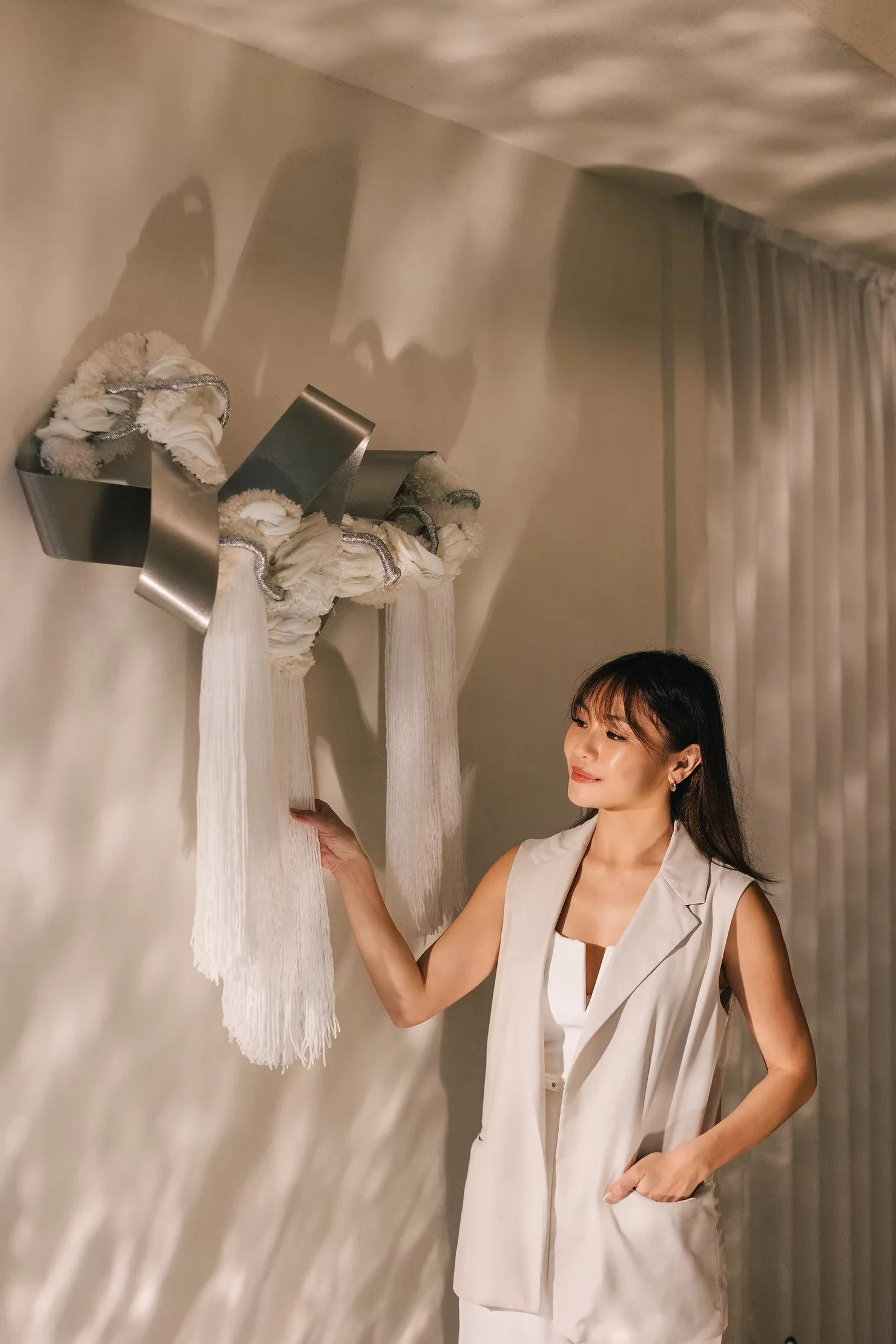 Curtains Singapore editorial image of a woman viewing contemporary fibre art beside soft curtains, with warm morning light and neutral interiors.