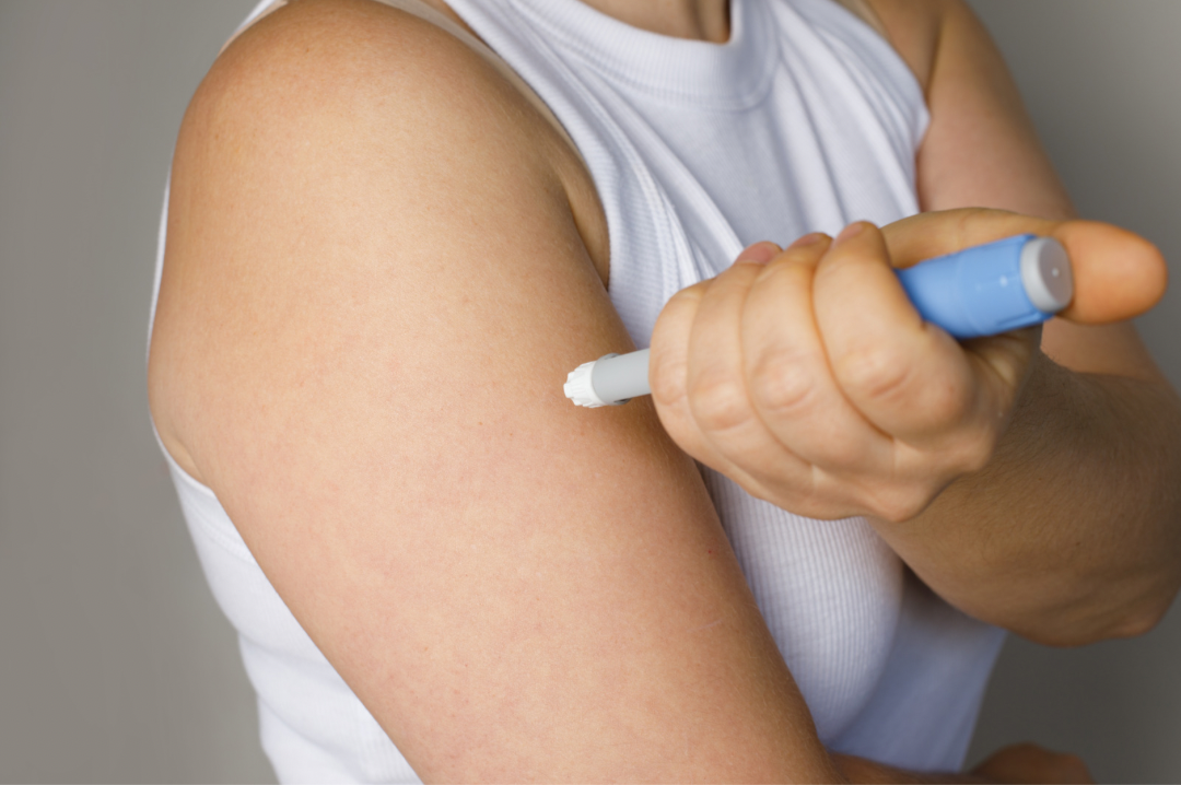 A person self-injecting into their upper arm with a blue pen injector, the way GLP-1 medicines are given.