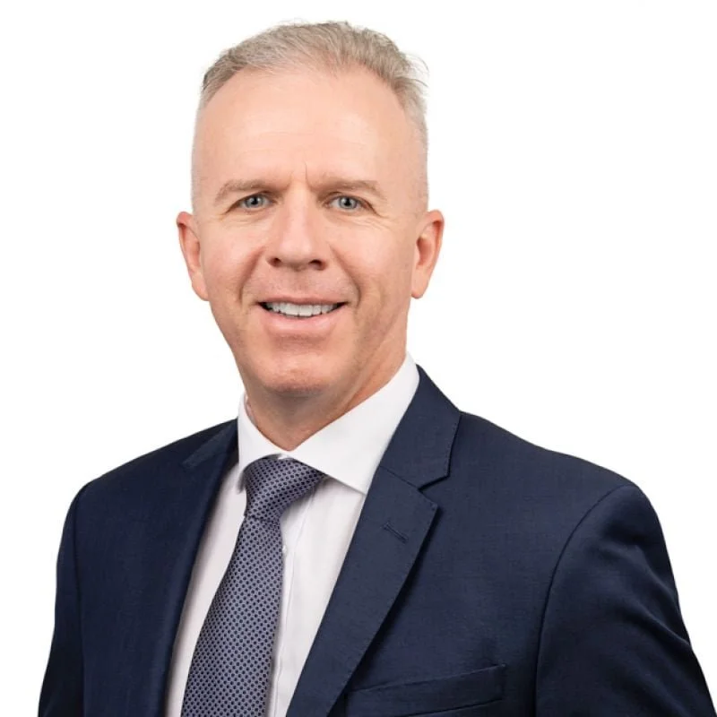 Professional headshot of a man with short blonde hair, wearing a dark suit, white shirt, and patterned tie, smiling against a white background. Craig Inkster from McGee's Property Darwin,