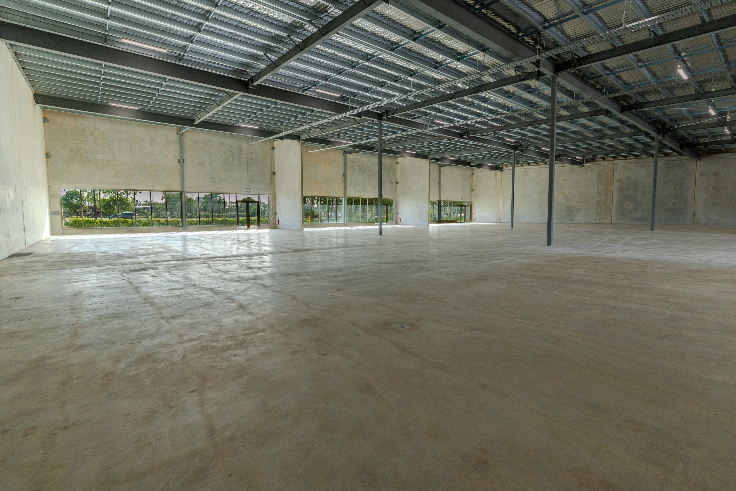Empty commercial space with concrete floor, large windows, and a metal ceiling under construction.
