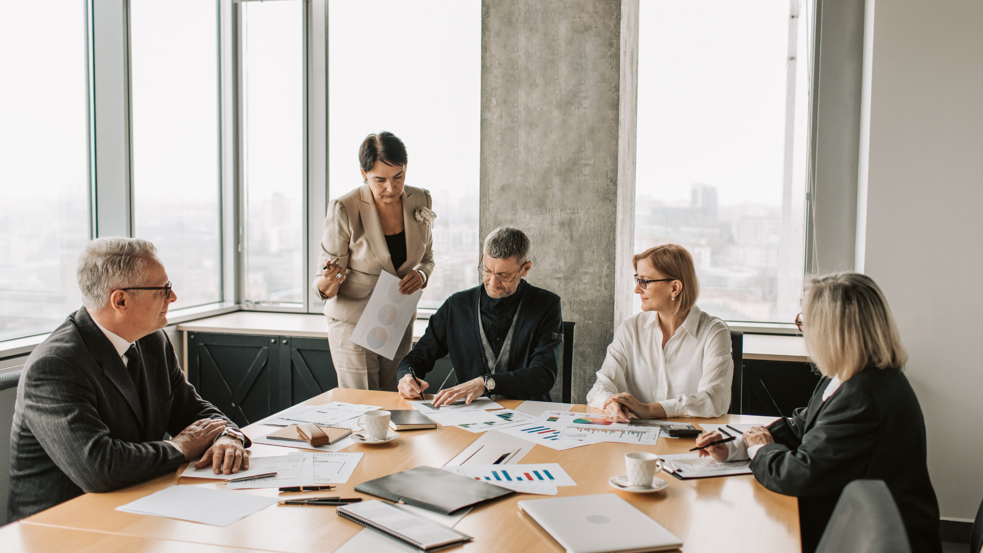 Business meeting with five diverse professionals around a table in a modern conference room with large windows